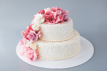 Obraz na płótnie Canvas Two-tiered white wedding cake decorated with pink flowers on a gray background. Cutout.
