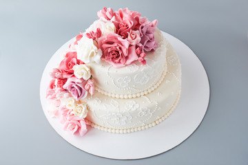 Two-tiered white wedding cake decorated with pink flowers on a gray background. Cutout.