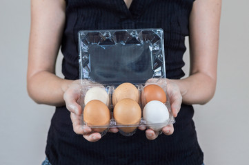 Caucasian woman with black shirt holding a plastic egg box full of chicken eggs