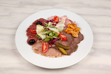 Sausage and meat with vegetables on a white plate with cutlery on the table.