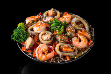 Soba Noodles (buckwheat) with seafood, shrimp, mussels, squid and vegetables: carrots, sweet peppers, broccoli on a black background. Sushi menu. Japanese food