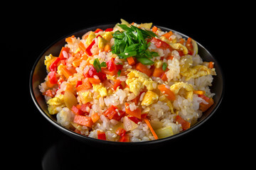 A plate of delicious rice with scrambled eggs and vegetables: carrots, sweet peppers, greens, spices and sauce on a black background