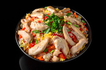 A plate of delicious rice with chicken in sauce and vegetables: carrots, sweet peppers, greens, spices on a black background