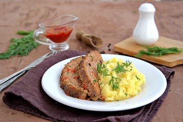 A meatloaf with mushrooms and red sweet pepper on a white plate with a garnish of mashed potatoes. Selective focus.