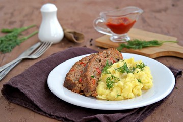 A meatloaf with mushrooms and red sweet pepper on a white plate with a garnish of mashed potatoes. Selective focus.