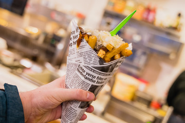 Human hand holding golden french fries wrapped in a newspaper with fresh onions