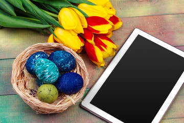 tablet screen for message and colorful tulips and easter eggs on wooden background