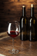 Bottle and glass of red wine on wooden barrel shot with dark wooden background