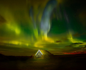 Night photo. Northern lights and a small house in the land overgrown with grass. Iceland.