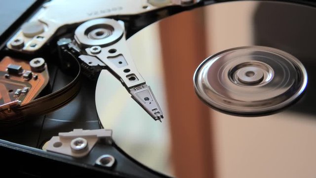 close up of interior of an hard disk drive writing data on the support with its head.