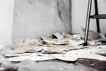 Rauhfasertapete wird von der Wand entfernt oder abgekratzt, Reste liegen auf dem Boden auf einer...