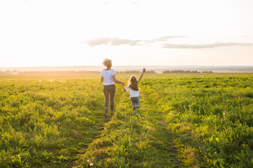 Family, summer and holiday concept - little daughter and mother run in the summer field