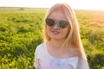 Indian holidays, fun and childhood concept - girl in glasses smiling, having fun on the holi festival