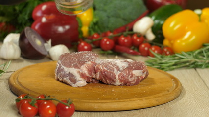 Chef with black gloves sprinkles meat lying on a wooden board with pepper, vegetables in the background, background blurred, side view