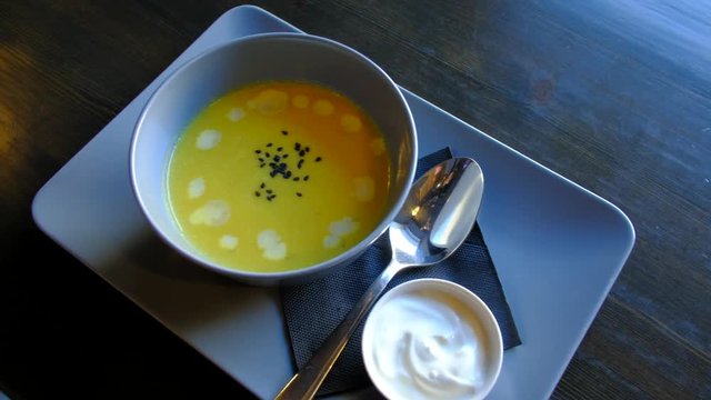 Top view - waiter delivers fresh pumpkin soup on the table in the restaurant. 4k.