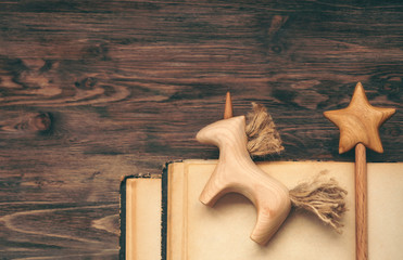 Wooden unicorn and wooden wand on beige shabby sheets. Old torn books. Soft light. Teal orange...