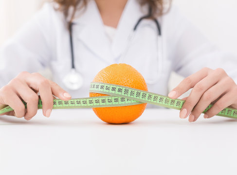 Doctor nutritionist holding measuring tape around orange