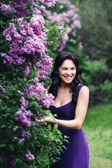 attractive cheerful woman in a purple dress laughing near the flowering bushes of lilac