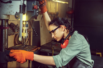 Busy and serious craftswoman grinding timbers with special machine. Beautiful woman wearing safety glasses. Concept of joiner's shop and woodworking. Gender equality. Male profession