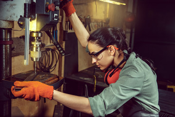 Busy and serious craftswoman grinding timbers with special machine. Beautiful woman wearing safety glasses. Concept of joiner's shop and woodworking. Gender equality. Male profession