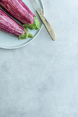  Teller mit gestreifte Auberginen zusammen mit einem Messer auf einem hellen grauen Hintergrund