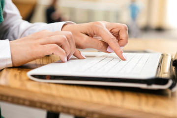 Woman typing on a laptop keyboard in a warm sunny day outdoors, sitting at the cafe table. Space for text