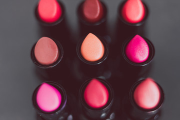 group of red pink and nude lipsticks lined up on dark table