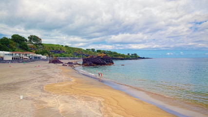 Fototapeta premium Sandy beach with black volcanic rocks at coast near the Vila Franca do Campo town, located on Sao Miguel island of Azores, Portugal.