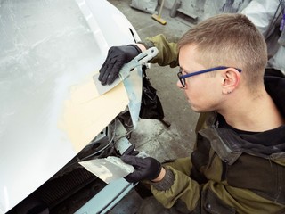 cute guy with glasses putty a car hood section of a garage in black gloves