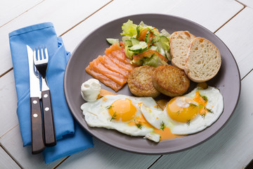 Breakfast if two fried eggs with salmon, hash browns
