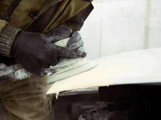 men's hands in black gloves polish the hood of the car with a pneumatic polisher in the garage