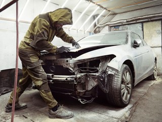 Cute guy in black glasses with black gloves displays the shape of the hood for the subsequent painting of the car. guy - a house painter working on a car in the garage