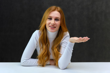 Concept portrait of a nice beautiful red-haired girl talking on a gray background in the studio sitting at the table.