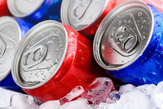 Red and blue soda cans on ice with condensation droplets