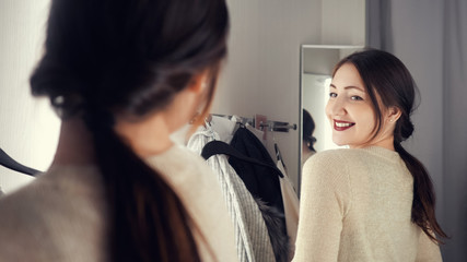 Young and happy brunette female in clothes store smiling and choosing new things. Boutique