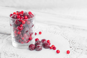 Frozen berries in a glass cup on the light wooden background. Cherry and cranberry