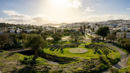 Myndos gate view of a bay of Bodrum, Mugla, Turkey. Beautiful sunset over the white houses and the archaeological ruins of the old city wall. Olive and palm trees