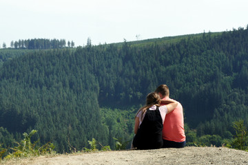 Naklejka na ściany i meble A pair of young people sitting over a mountain valley. 