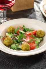 Vegetarian green salad with falafel and glass of red wine on the table