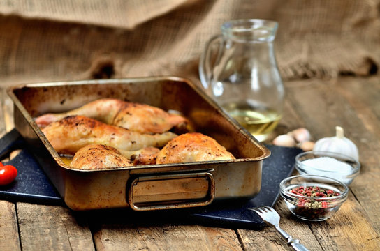 Golden Roasted Chicken Legs In A Baking Pan, Pepper, Salt, Garlic, Cherry Tomatoes, Fork And Jug With Oil In The Background