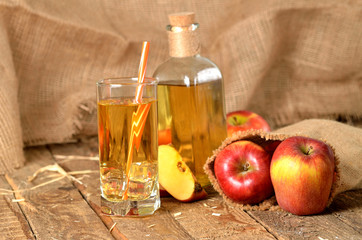 Juice from fresh apples, straw, ice and bottle in background on wooden boards