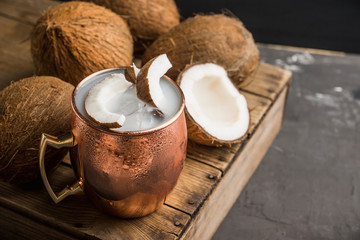 Sweet coconut cocktail in copper mug (variation of Moscow mule) on the wooden background. Selective focus. Shallow depth of field. 