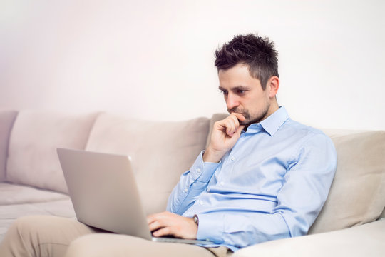 Upset and worried young businessman sitting and working at laptop