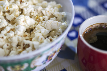 A cup of coffee and popcorn in a bowl. Closeup top view