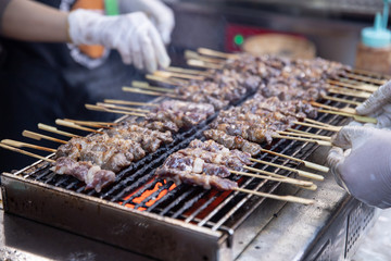 seller grilling tasty bbq meat with wooden skewers on fire.