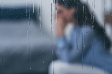 selective focus of raindrops on windows with sad woman sitting on background