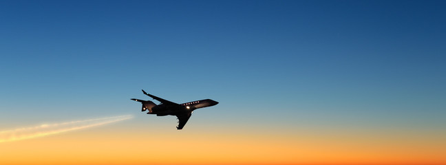 business jet airplane flying on beautiful sunset sky landscape background at dusk dawn time scenic aerial up silhouette plane view corporate air travel concept wide panorama banner - obrazy, fototapety, plakaty