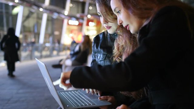  Two young women at night outdoor using laptop computer &ndash; business world, collaborating, planning concept