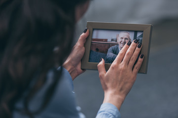 cropped view of woman holding photo frame with mature man at home, grieving disorder concept