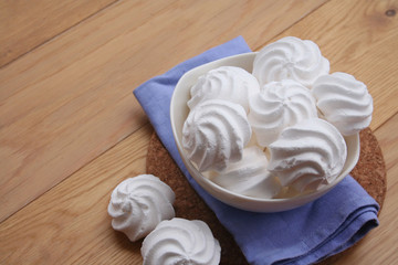 Small white meringues in a bowl on wooden table